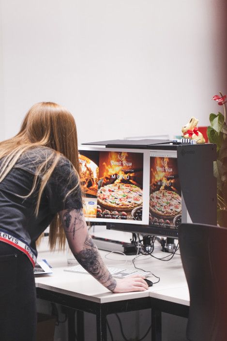 Druckvorstufenmitarbeiterin beim Vergleichen eines Ausdruckes gegenüber einem kalibrierten Bildschirm